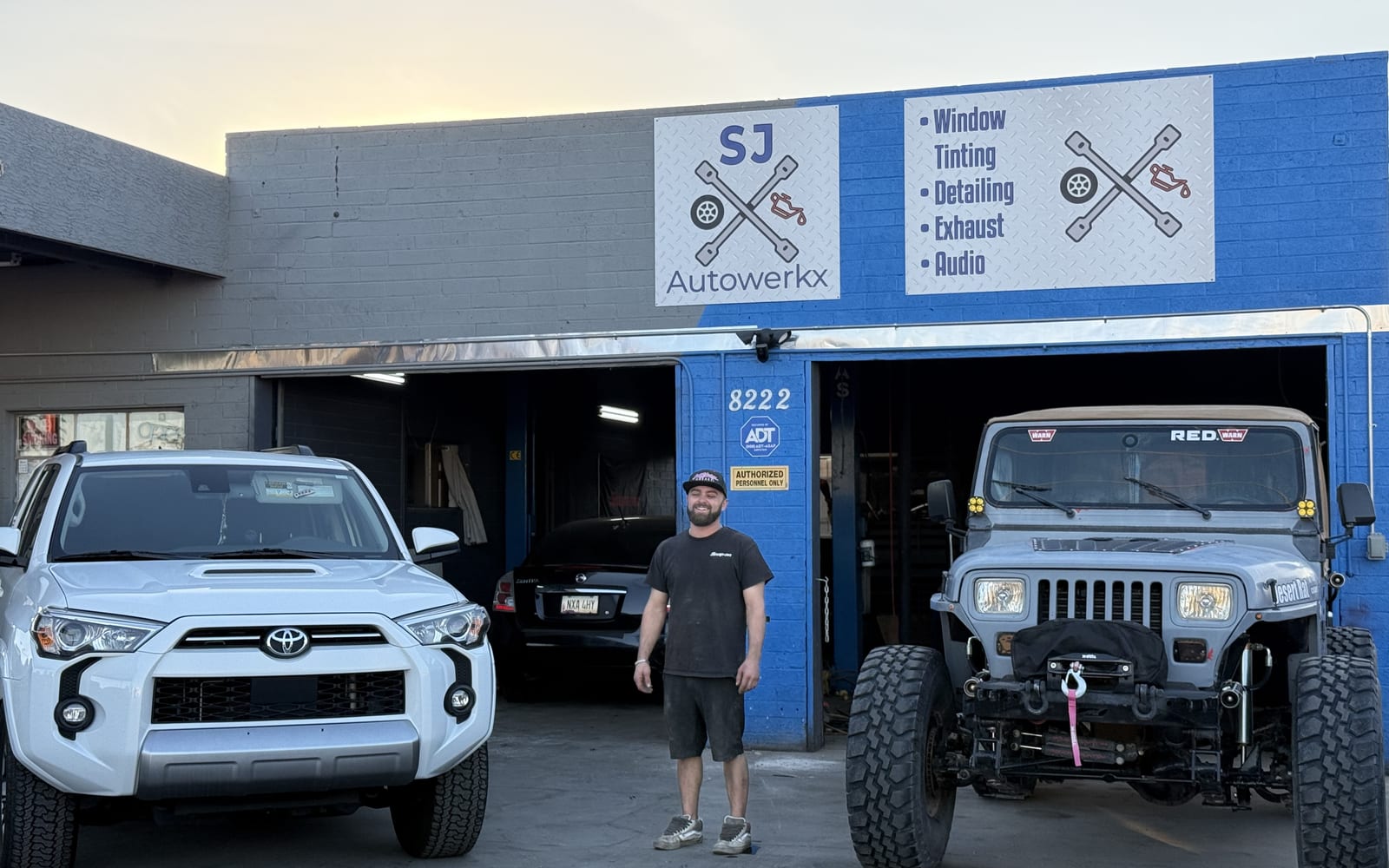 Owner Scott Coburn standing outside the SJ Autowerkx shop bays in Guadalupe, Arizona, between a Toyota 4Runner and a lifted Jeep Wrangler.